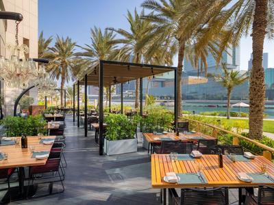 Außenbereich eines Restaurants mit Tischen und Stühlen unter Palmen und Blick auf einen Pool.