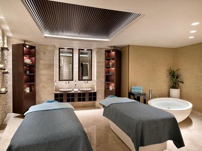 Eleganter Spa-Raum mit zwei Massageliegen, Wanne und stilvoller Beleuchtung.