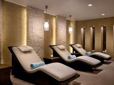 Drei moderne Liegestühle mit weißen Polstern in einem ruhigen, stimmungsvoll beleuchteten Wellnessraum.