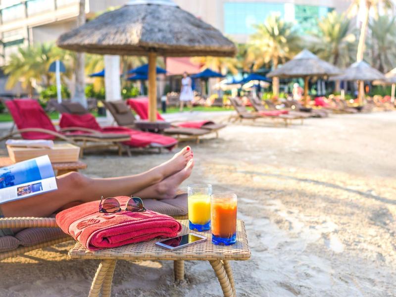 Liegestühle mit bunten Handtüchern, frischen Säften und einer Person am Strand unter Sonnenschirmen.