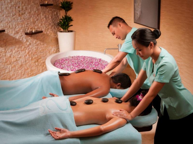 Zwei Personen erhalten Wellness-Massage mit heißen Steinen in warm gestaltetem Spa-Raum.