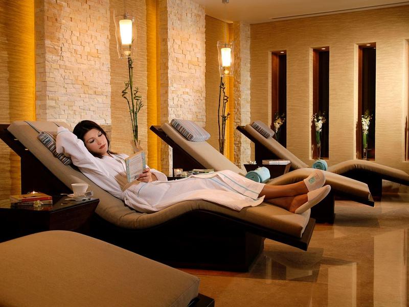 Frau entspannt auf hellbraunem Liegestuhl in gemütlichem, warm beleuchtetem Wellnessraum.