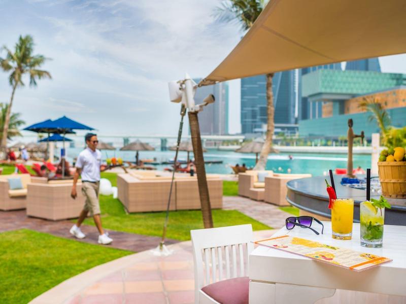 Freizeitbereich mit Liegestühlen, Getränken und Palmen an einem sonnigen Tag am Wasser.