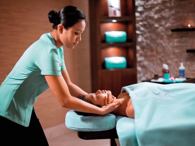 Eine Frau massiert entspannt den Kopf einer liegenden Person auf einer Behandlungsliege.