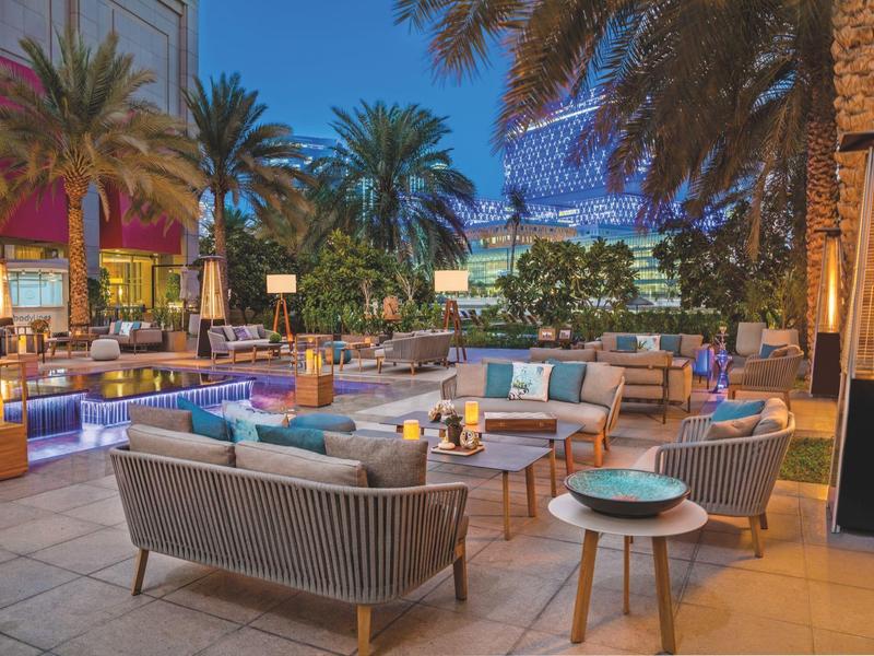 Moderner Außenbereich mit Sofas, Tischen, Palmen und stimmungsvoller Beleuchtung bei Nacht.