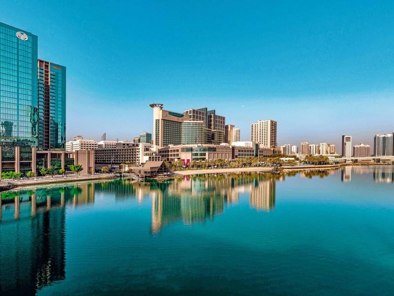 Stadtansicht mit modernen Hochhäusern und deren Spiegelung im klaren, ruhigen Wasser.