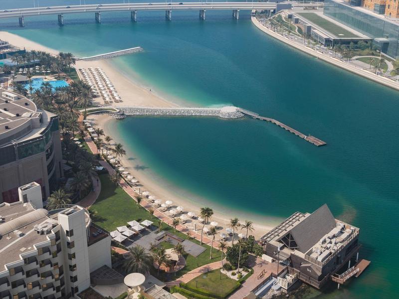 Strand mit feinem Sand, klarem türkisblauem Wasser und umliegender moderner Gebäudearchitektur.