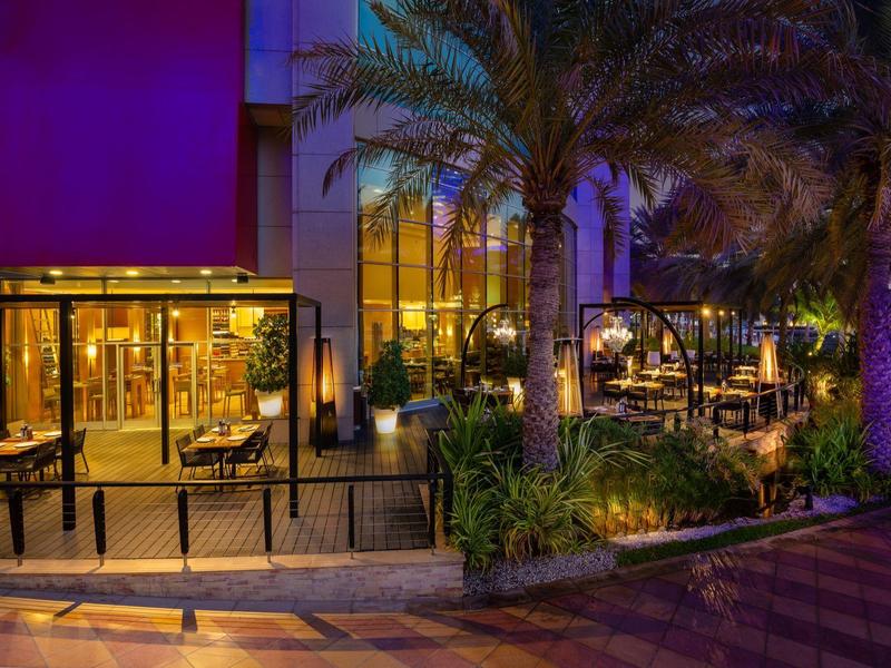 Außenbereich eines Restaurants nachts, beleuchtet mit warmem Licht und umgeben von Pflanzen.