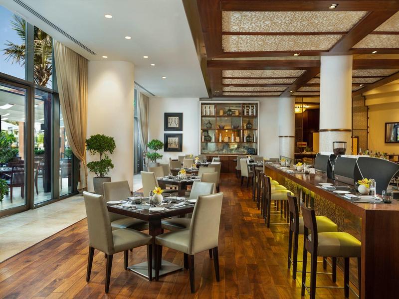 Modernes Restaurant mit Holzboden, Sitzgruppen, Barhockern und großen Fenstern zur Außenterrasse.