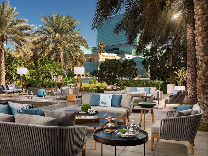 Outdoor-Lounge mit modernen Sitzgruppen, Palmen und blauem Himmel in entspannter Atmosphäre.