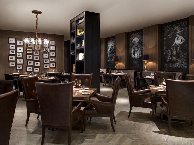 Elegantes Restaurant mit dunklen Holzmöbeln, Lederstühlen, großem Kronleuchter und Wandkunst.