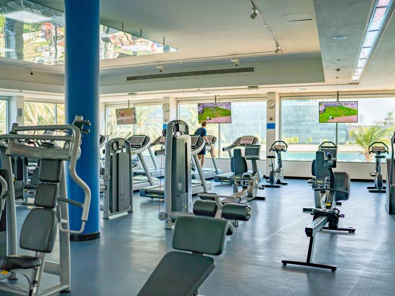 Moderner Fitnessraum mit Cardio- und Kraftgeräten, großen Fenstern und heller Raumbeleuchtung.