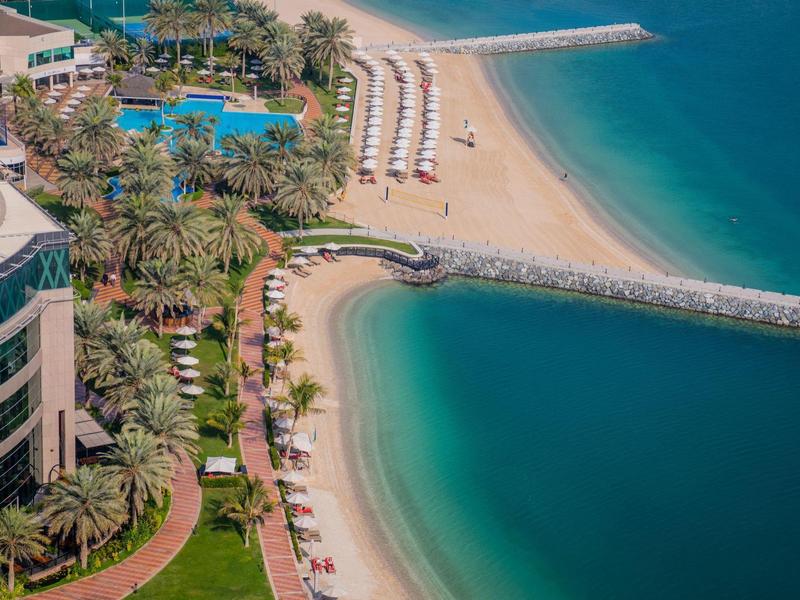 Luxuriöser Strandbereich mit Pools, Palmen, Liegestühlen und klarem türkisem Meer.