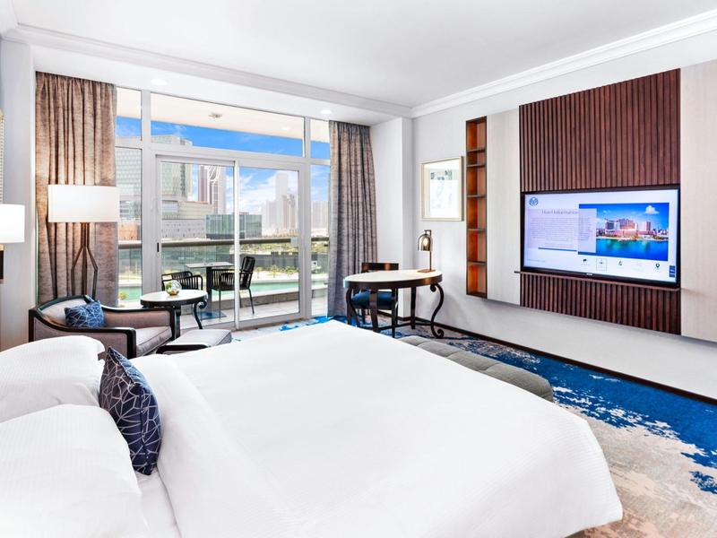 Modernes Hotelzimmer mit großem Bett, Schreibtisch und Balkon mit Stadtblick.