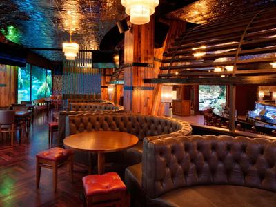 Gemütliche Bar mit braunen Ledersofas, runden Holztischen, Stühlen und gedämpfter Beleuchtung.