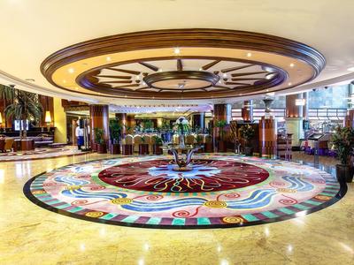 Große Hotel-Lobby mit glänzendem Marmorboden, farbigem Mittelornament und stilvoller Deckenbeleuchtung.