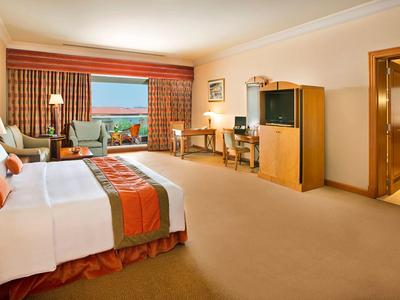 Großes Hotelzimmer mit hellen Wänden, Doppelbett, TV, Schreibtisch und Blick auf das Meer.