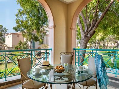Terrasse mit Glastisch und Stühlen, umgeben von Bäumen und buntem Geländer