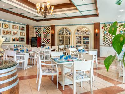 Helles Restaurant mit weißen Holzmöbeln, Terrakottaboden und dekorativem Weinfass.