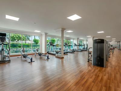 Großer Fitnessraum mit modernen Geräten und Holzboden, hell durch Fenster mit Blick auf Grünfläche.