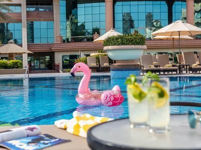 Poolbereich mit Liegen, Sonnenschirmen und einem pinken Flamingo-Schwimmreifen in klarem Wasser