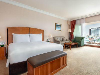 Helles Hotelzimmer mit Doppelbett, Sofa, Sessel und Balkon mit Blick nach draußen.