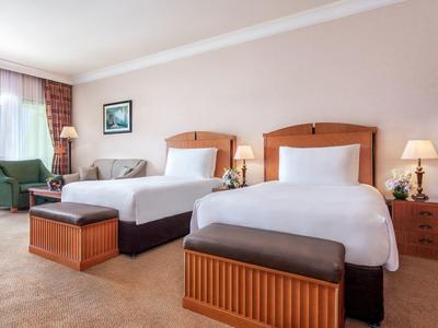 Hotelzimmer mit zwei Betten, Nachttischen, einer Sitzbank und einem Sessel am Fenster