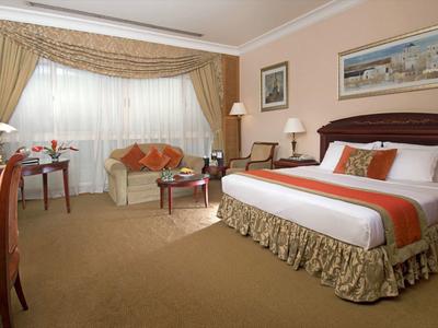 Gemütliches Hotelzimmer mit großem Bett, Sofa, Schreibtisch und warmen Beige- und Brauntönen.