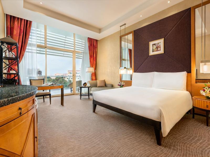 Helles Hotelzimmer mit großem Bett, zwei Sesseln und Fenster mit Stadtblick.