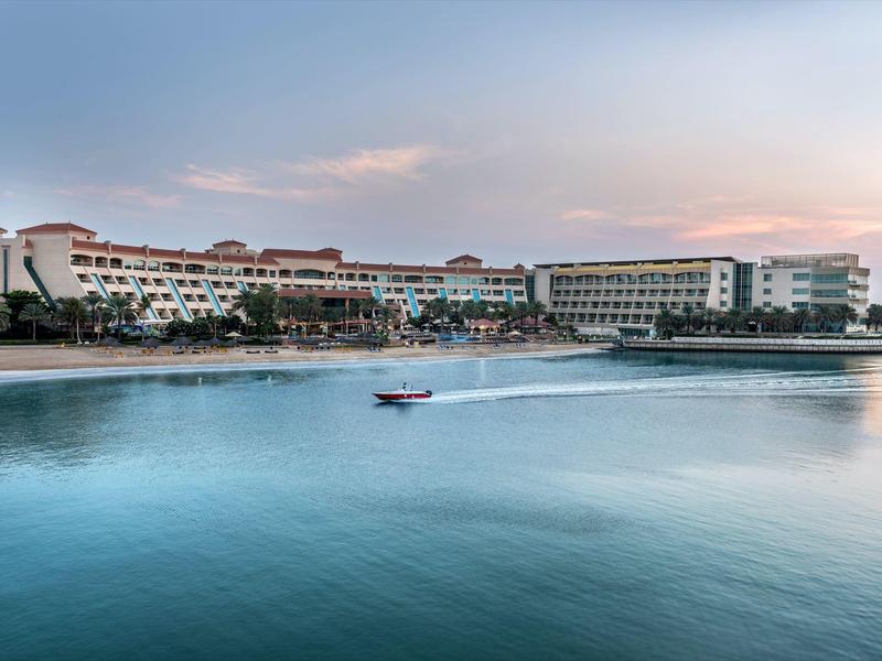 Großes Hotel am Wasser mit Boot im Vordergrund bei Sonnenuntergang