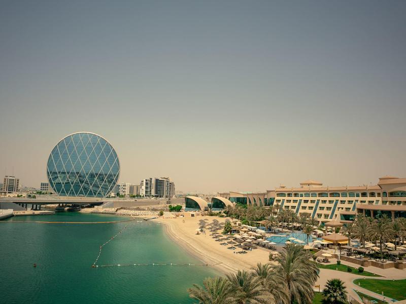 Strand und Hotel mit Pools neben einem kreisförmigen modernen Gebäude am Meer.
