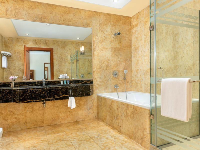 Elegantes Badezimmer mit Marmorfliesen, Badewanne, Dusche und Doppelwaschbecken in einem Hotelzimmer.