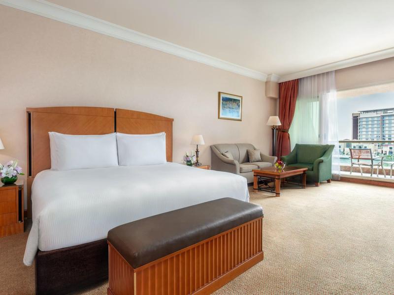 Helles Hotelzimmer mit Doppelbett, Sofa, Sessel und Balkon mit Blick nach draußen.