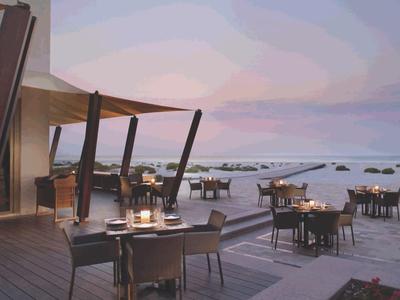 Offenes Restaurant mit Tischen am Strand und Blick auf das Meer bei Sonnenuntergang.