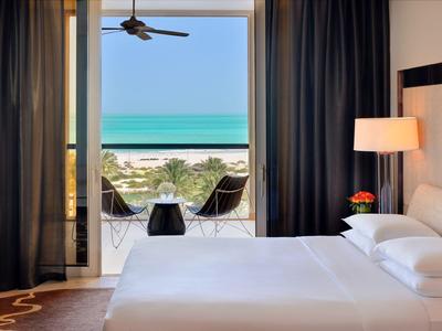 Modernes Hotelzimmer mit Doppelbett und Balkon mit Blick auf Strand und Meer.