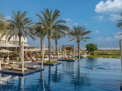 Luxuriöser Poolbereich mit Palmen und Liegen unter blauem Himmel