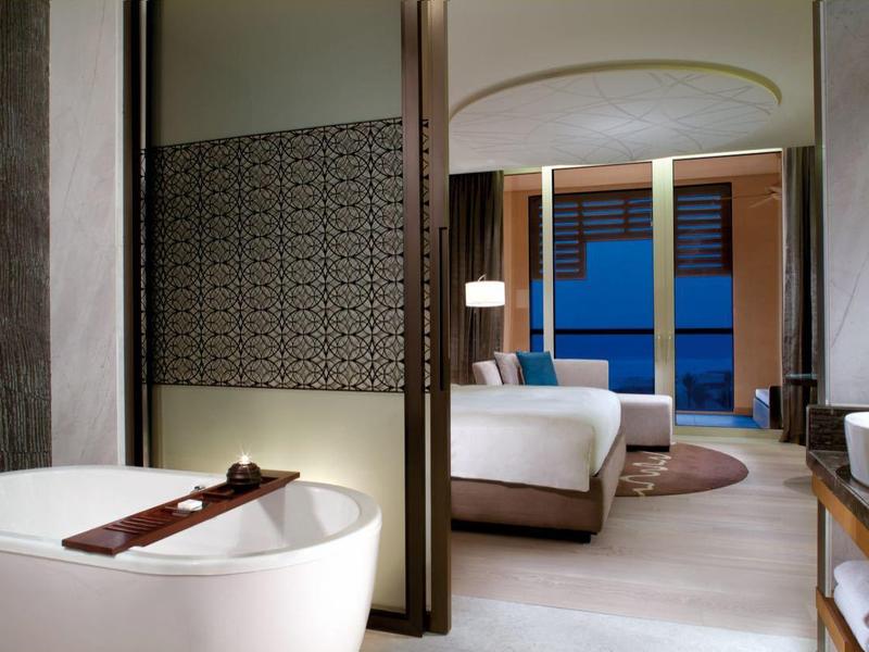 Modernes Hotelzimmer mit Badewanne, Doppelbett, großen Fenstern und elegantem, hellgrauem Design.