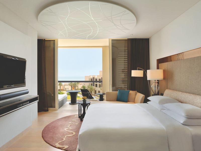 Modernes Hotelzimmer mit großem Bett, Fernseher, Balkon und Stadtblick bei Tageslicht.