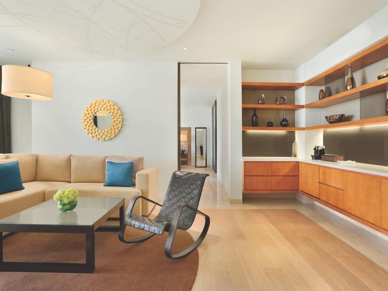 Helles Wohnzimmer mit beige Sofa, Holzregalen, schwarzem Stuhl und großem Spiegel an weißer Wand.