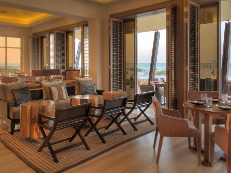 Einladender, hell erleuchteter Restaurantraum mit Holzmöbeln und Meerblick durch große Fenster.