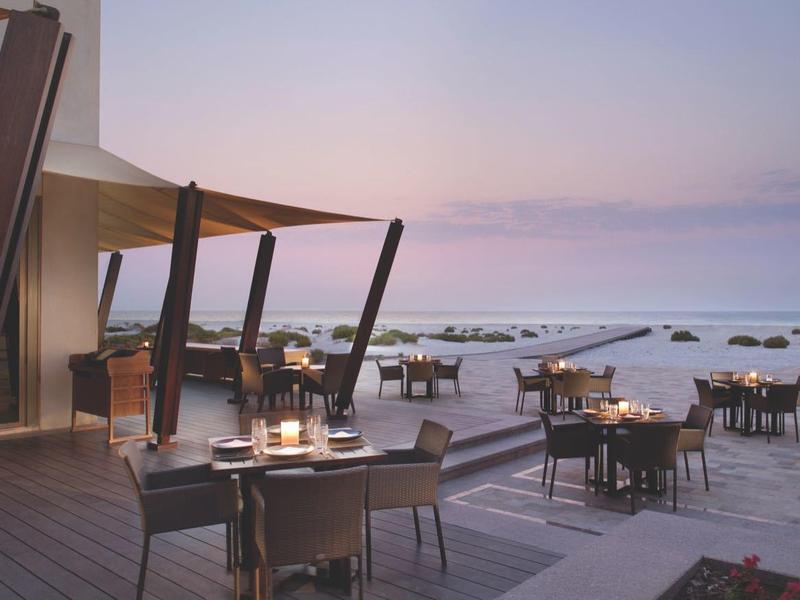 Strandrestaurant bei Sonnenuntergang mit gedeckten Tischen auf Holzterrasse und Blick aufs Meer.