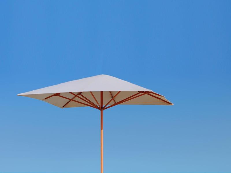 Zwei Sonnenliegen mit weißem Sonnenschirm am Sandstrand vor blauem Meer und klarem Himmel.