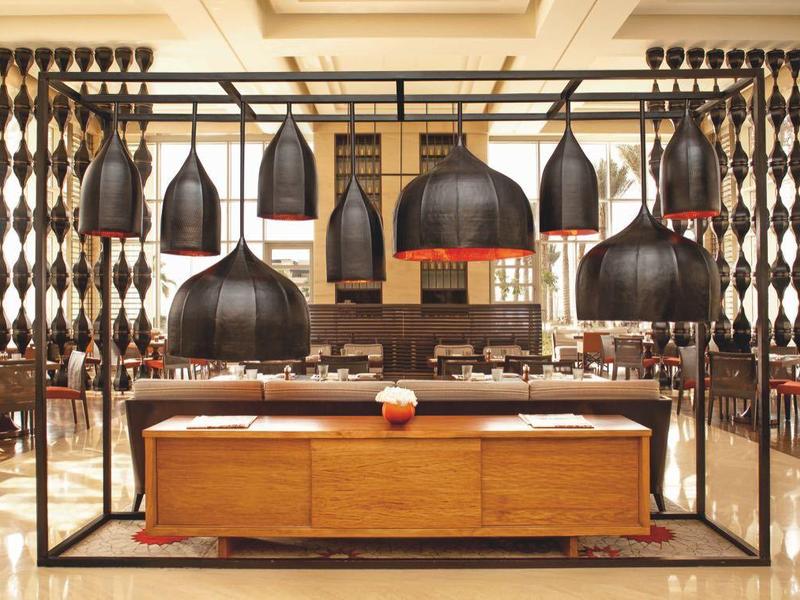 Moderner, heller Gastraum mit braunen Holztischen, schwarzen Lampen und großen Fenstern links und rechts.