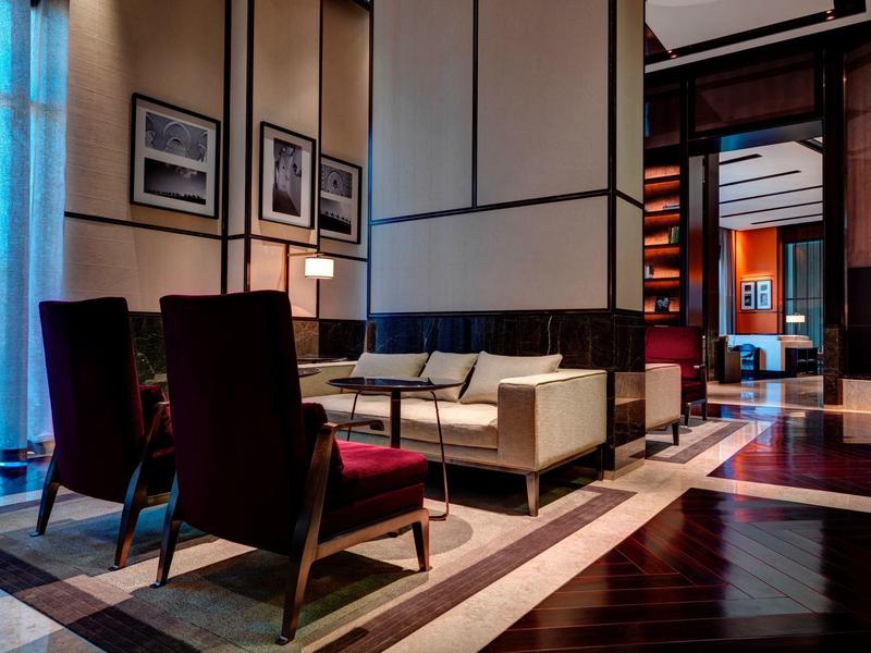 Eleganter Wartebereich mit dunkelroten Sesseln, weißem Sofa, modernen Lampen und gehäkeltem Teppich.