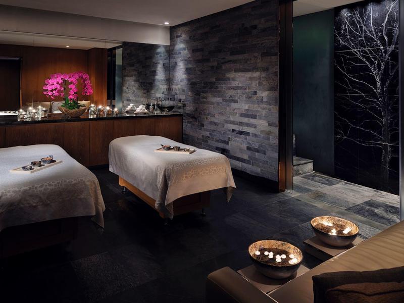 Dunkler Wellnessraum mit zwei Massageliegen, Kerzen und stimmungsvoller Beleuchtung.