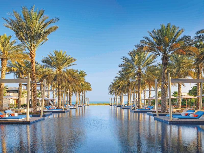 Luxuriöser Pool mit blauen Liegen und Palmen unter klarem Himmel am Meer.