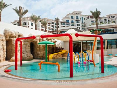 Aire de jeux aquatique colorée avec toboggans et arroseurs devant un hôtel avec des palmiers.