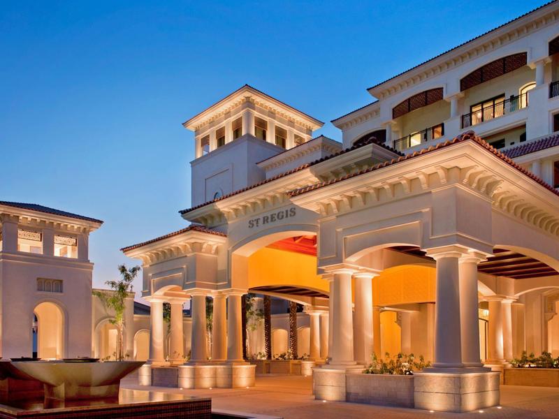 Eleganter Hoteleingang mit beleuchteten Säulen unter blauem Abendhimmel.