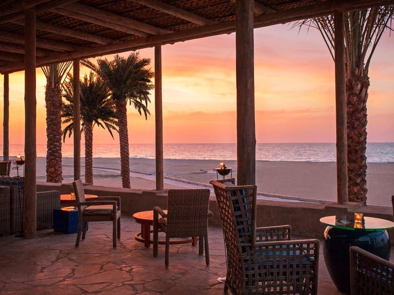 Sitzbereich unter überdachtem Strandrestaurant mit Blick auf Sonnenuntergang und Meer.