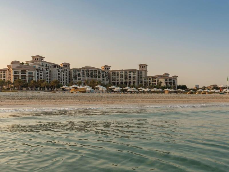 Hotelkomplex am Strand bei Sonnenuntergang mit ruhigem Wasser im Vordergrund.